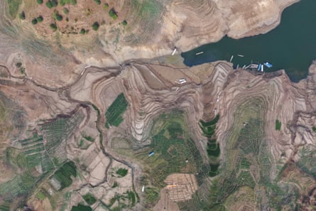 Aerial view over dry reservoir with small areas and streams of water amid mud, silt or sand.