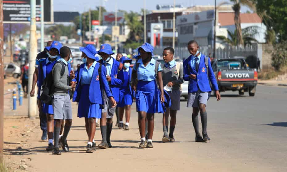 Children in a blue uniform walk along a main road