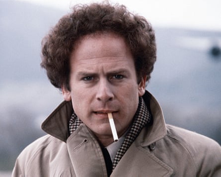 Art Garfunkel in a trenchcoat with the collar up, unlit cigarette in his mouth