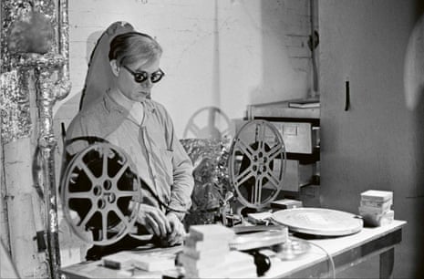 Warhol in his studio with reels of film on a table in front of him