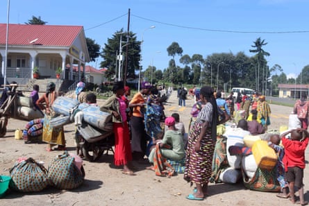 A group of African women on the street in a town with bed rolls, jerry cans and bags of other belongings