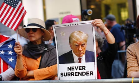 Person holds sign obscuring face that is Trump mugshot with words Never Surrender.