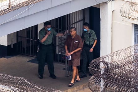 A prisoner walks between two prison guards behind razor wire