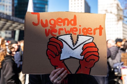 A protest sign in German with an image of two hands tearing an envelope apart