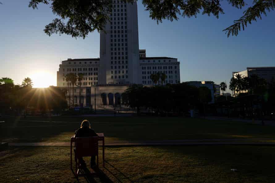 A homeless man sits in the morning sun in downtown Los Angeles in front of city hall.