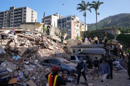 Residents and rescue workers search through a large pile of rubble