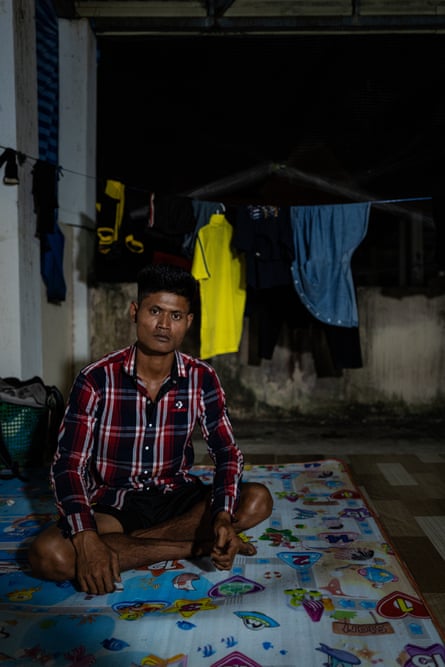 A grim-faced south-east Asian man sits cross-legged on a mat at night
