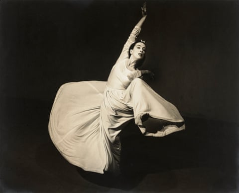 a black and white photo of a woman dancing in a long white gown on a dark background