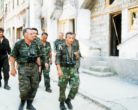 Mladić, in combat fatigues, walks along a street at the head of a group of soldiers
