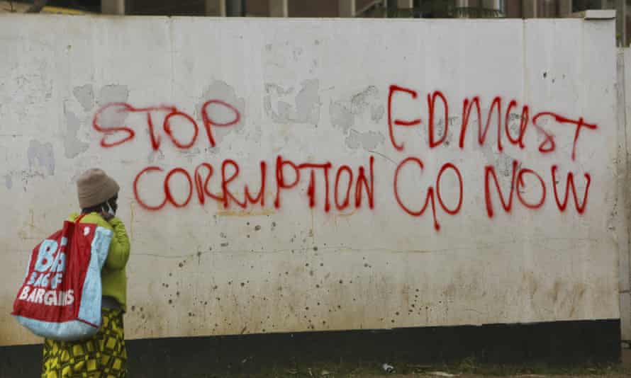 A woman in Zimbabwe walks past a wall with graffiti calling on the government to stop corruption June 2020.