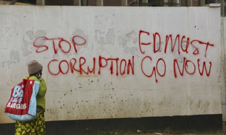 A woman in Zimbabwe walks past a wall with graffiti calling on the government to stop corruption June 2020.