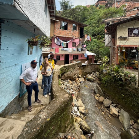 A group of people stand on a narrow residential street behind a low wall looking at a river.