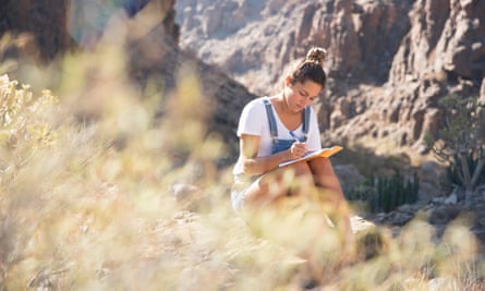 Young female hiker writing notes in rocky valley