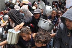 People jostle and hold out pots and pans for food