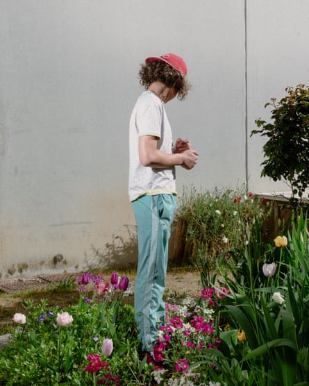 A boy wearing a red cap stands among flowers