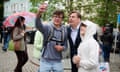 Maximilian Krah, in a shirt and suit jacket and holding a shopping bag printed with "AfD", poses with two young men as one holds up his phone for a selfie