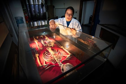 A woman in a lab coat inspects a skeleton that is under glass