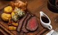 A plate of food on a board including picanha steak, roast potatoes, carrots and yorkshire pudding, with a gravy boat