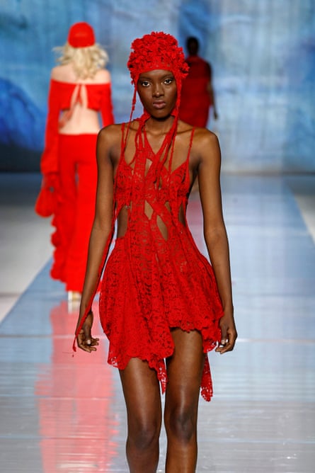 A model walks the runway wearing a short, lacey red dress