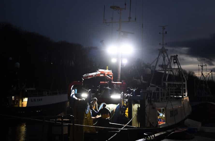 Workers unload a trawler under lights at night