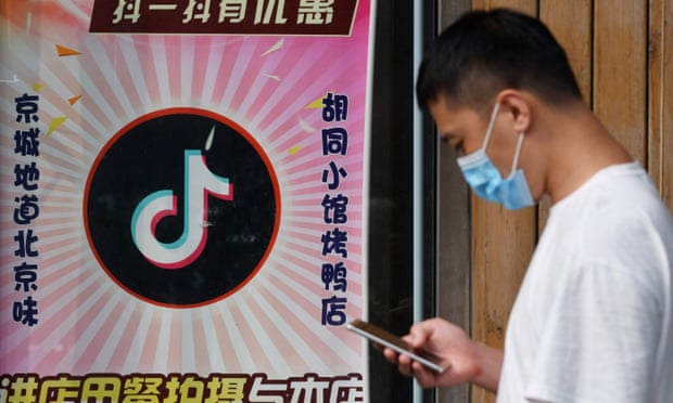 A man looking at his phone walks past a restaurant in Beijing displaying a TikTok logo