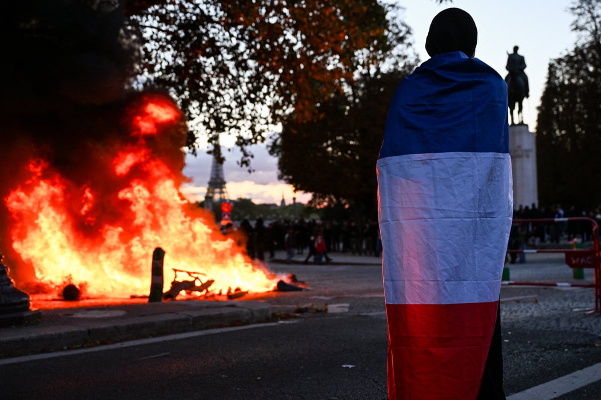 A protester covered with the French flag stands next to a fire while looking at the Eiffel Tower in the background during a demonstration against the "high cost of living", in Paris on Saturday.