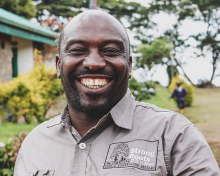 Dominique Bikaba smiling in a head and shoulders photo against a backdrop of garden and trees around a building