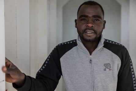 A man wearing a grey tracksuit with black sleeves looks at the camera.