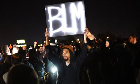 A man stands among a crowd of people holding a sign that reads 'BLM'.