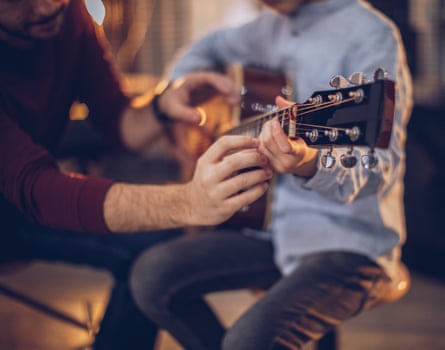 A child holding a guitar with a man helping to place his fingers on the strings