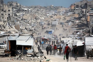 Palestinians carry bags as they walk down a street of bombed and flattened buildings