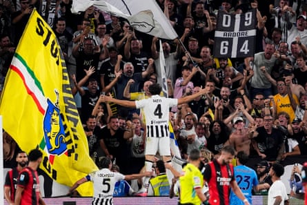 Federico Gatti stands on a hoarding in front of the crowd with his arms stretched wide after levelling for Juventus.