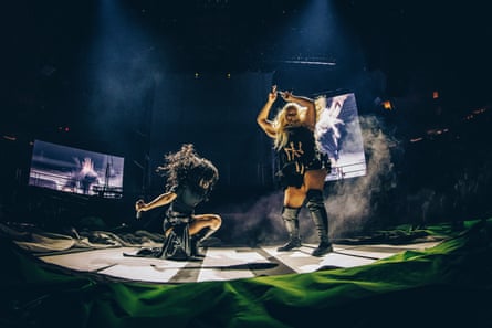 The two artists dancing, spotlit on a darkened stage with video screens behind them