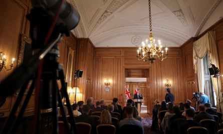 Long distance shoy from the back of the room of Keir Starmer speaking at a podium in a wood-panelled room
