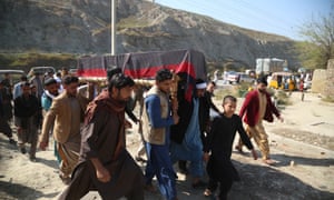 A group of Afghan pallbearers carry a coffin covered in a drape across rough ground with a line of mountains in the background