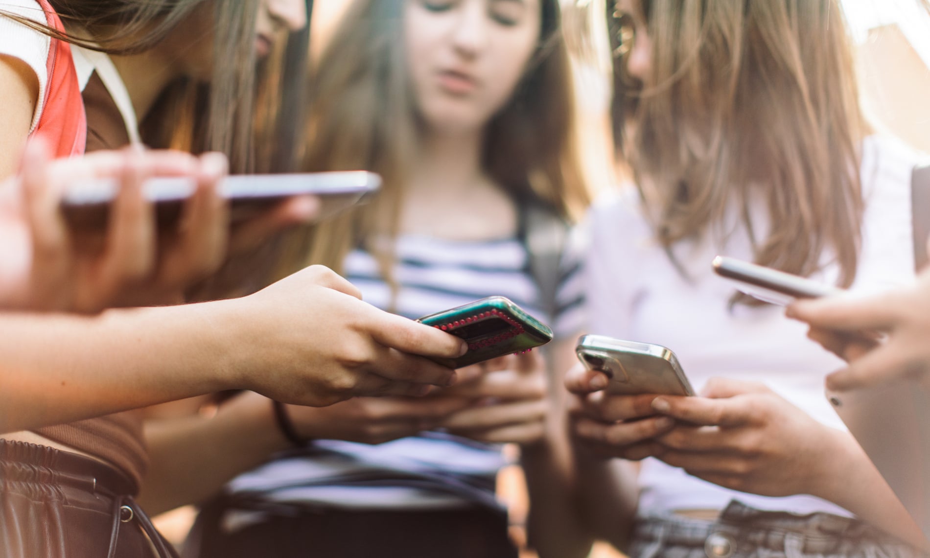 Grupo de adolescentes utilizando sus teléfonos móviles en un entorno al aire libre, representando el uso frecuente de redes sociales entre jóvenes.