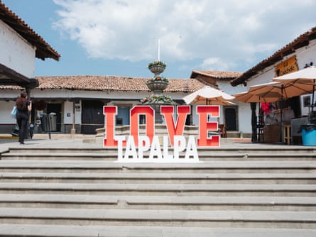 Large letters spelling ‘Love Tapalpa’ on steps, with colonial-style buildings and a fountain in the background