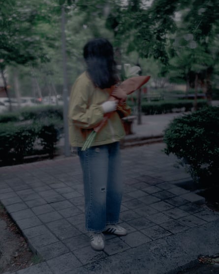 Blurry image of a woman, her face obscured, in a public garden holding a bunch of flowers