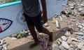 A child carries a surfboard, the ground is strewn with rubbish