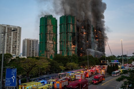 Emergency vehicles parked in a road as smoke and flames rise in the background