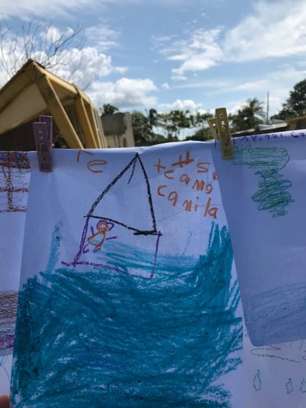 Children’s drawings of houses hang on a line, attached with pegs, with damaged buildings in the background