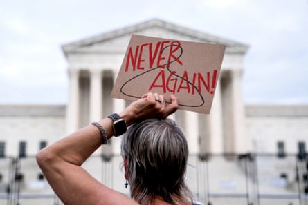 A person holds a sign that reads “never again” with a white-columned grand building in the background.