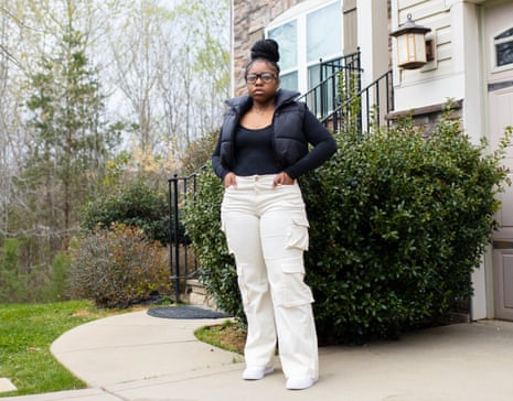 Woman in white pants and black jacket stands for a portrait in front of a home