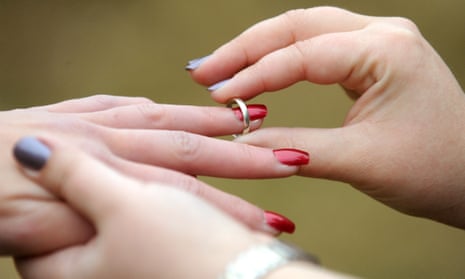 A woman places a wedding ring on her partner’s finger.