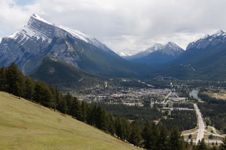 Banff, Alberta, sits in a forested valley surrounded by snow-capped mountains under a cloudy sky