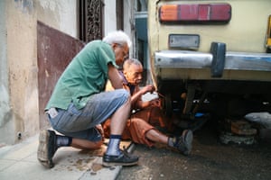 Two older men work on the wheel of an old Lada in a street in Havana.