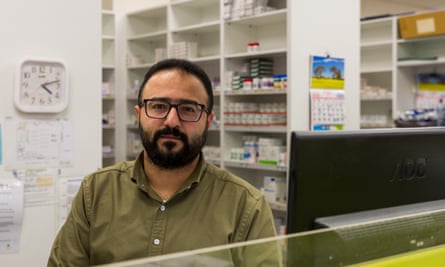 Mena Shawky sitting behind a computer screen in front of shelves of medication