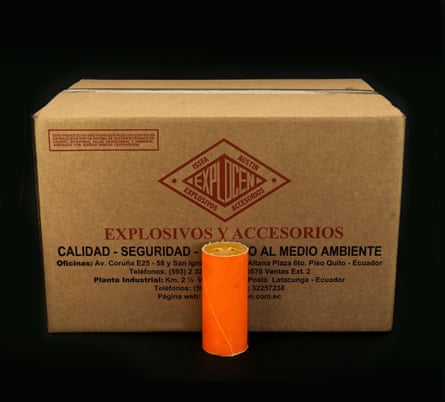 An orange cylinder, like a stick of dynamite, in front of a box marked ‘explosives’ in Spanish
