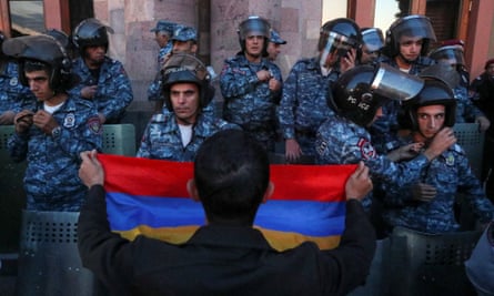 ایک شخص نے ایک عمارت کی حفاظت کرنے والے فوجی اہلکاروں کے ڈبل رینک کے سامنے سرخ، نیلے اور نیلے رنگ کا ترنگا پرچم اٹھا رکھا ہے۔