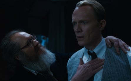 A man with a grey beard and glasses holding a man with short blond hair in a grey waistcoat, white tie and white shirt